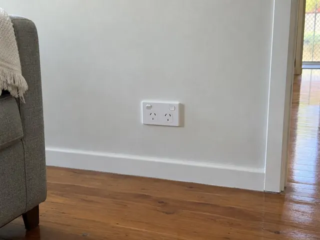Double power point on a painted wall above timber flooring in a home interior in Carrara
