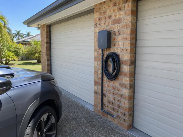 Wall-mounted EV charger with coiled cable on a brick garage wall beside closed doors in Ashmore